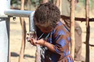 El rol de las mujeres en la gestión del agua: niña bebiendo agua de un pozo