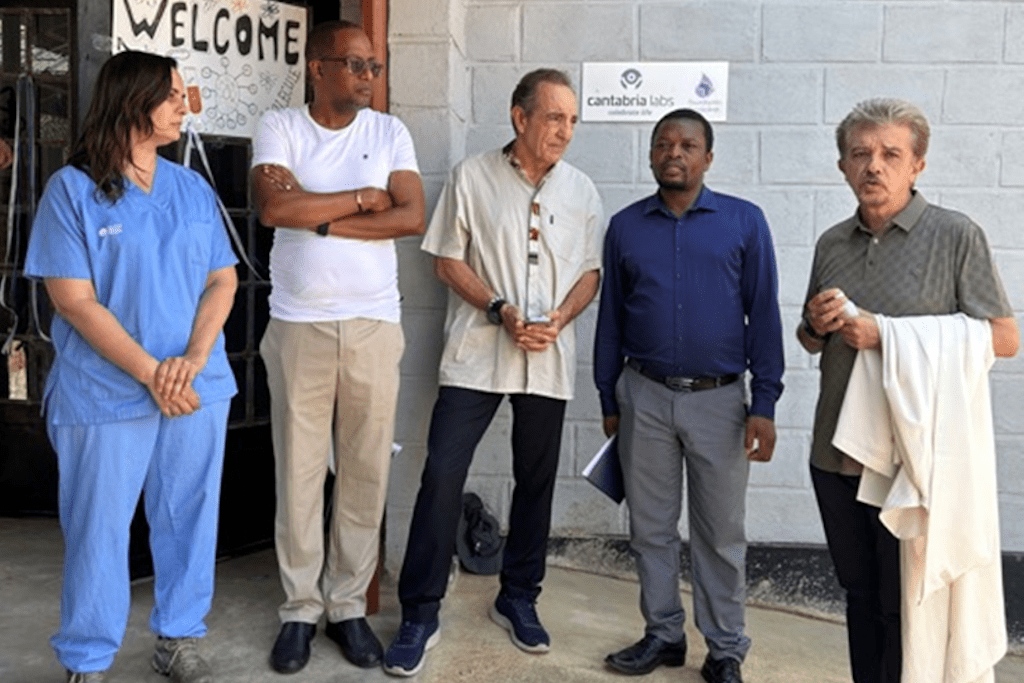 Five people stand in a row outside a building; a nurse in blue scrubs is on the left, with others in casual and business attire, and a Welcome sign with a Cantabria Labs logo in the background.