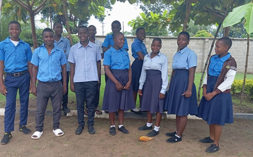 Group of students in blue school uniforms posing outdoors in a yard.
