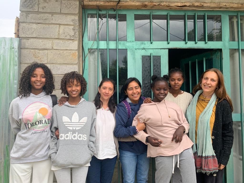 Group of diverse young women and girls posing together outdoors in front of a green doorway, smiling at the camera.