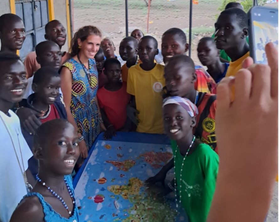 Group of smiling people of diverse ages gathered around a colorful world map on a table, posing for a photo.
