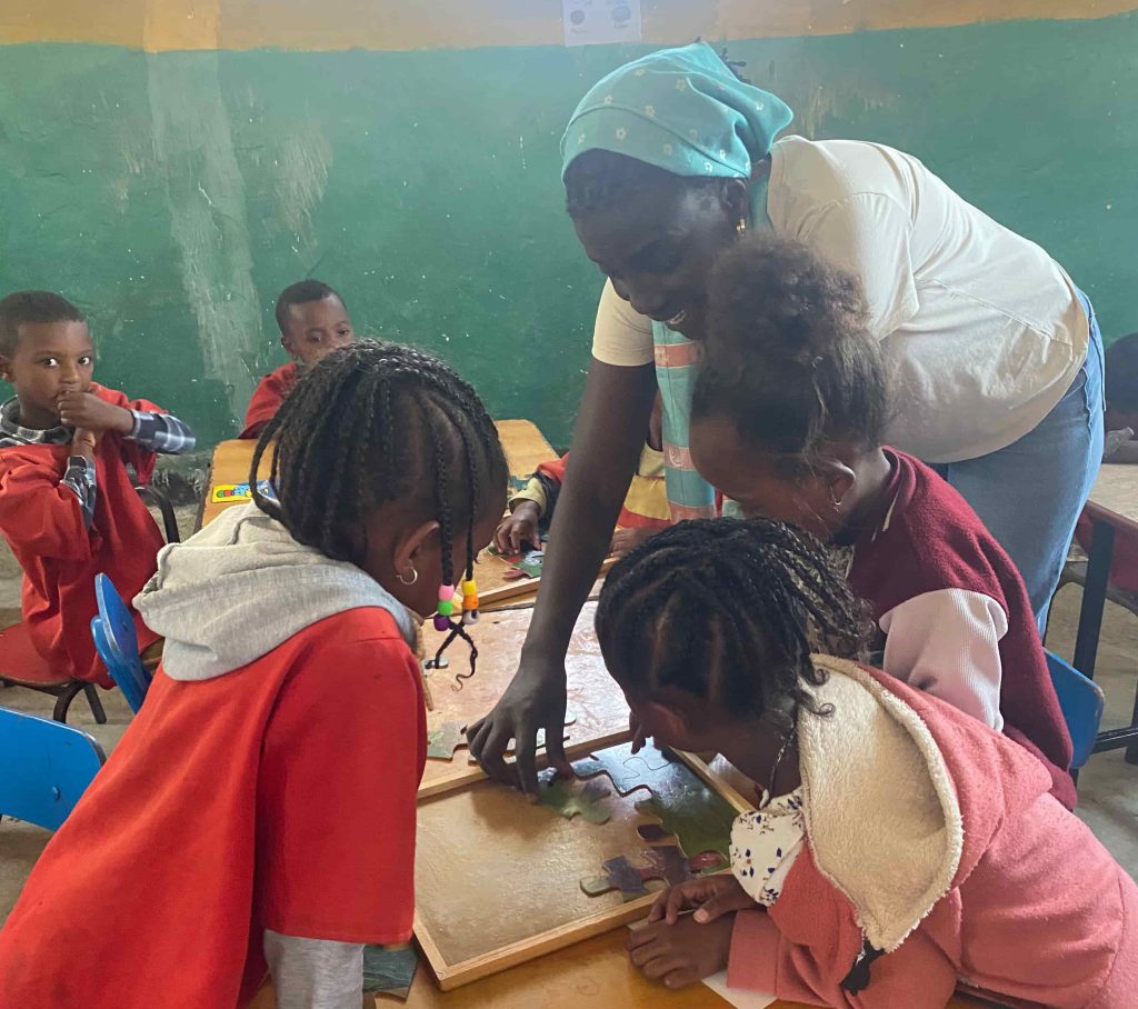 Children and adults gathered around a wooden puzzle table in a classroom, working on a colorful puzzle together.