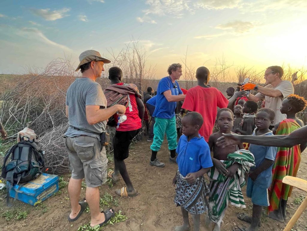Group of adults and children outdoors at sunset, volunteers distributing supplies.