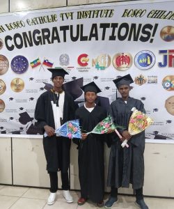 Three graduates in caps and gowns pose indoors in front of a large "CONGRATULATIONS!" banner, each holding a bouquet of flowers.