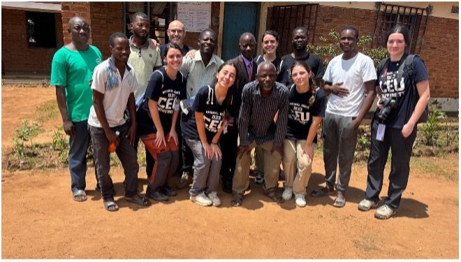 Diverse group of adults posing outside a brick building, some wearing matching black shirts, smiling for a team photo.